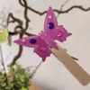 A close-up of a purple butterfly decoration attached to a wooden clothespin, which is clipped onto a branch. Podgląd zdjęcia produktu