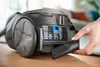 A hand is shown inserting a crevice tool into the side of a black bag vacuum cleaner. Produktbild-Vorschau
