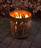 A rusty metal fire pit with flames burning inside, placed on a paved patio with fallen leaves in the background. Produktbild-Vorschau
