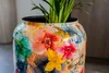 A close-up of a decorative flower-patterned pot with a plant inside. Voir les images du produit