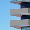 A close-up view of a modern building's balconies with grey privacy screens against a clear blue sky. Produktbild-Vorschau