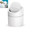 A small white trash can with a lid, shown on a white background. A smaller inset image shows the trash can on a desk with some nuts and papers. Produktbild-Vorschau