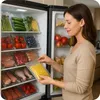 A woman is putting a bag of corn into a refrigerator filled with vacuum-sealed food. Podgląd zdjęcia produktu