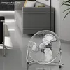 A chrome floor fan is placed in a modern living room setting, with a grey sofa and decorative pillows in the background. Náhľad obrázku produktu