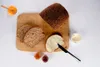 A loaf of bread, sliced bread, butter, jam, and honey are arranged on a wooden cutting board. Produktbild-Vorschau