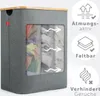 A grey fabric laundry basket with a wooden lid and three transparent mesh compartments filled with laundry. It is shown against a white background with marketing icons and text on the right side. Produktbild-Vorschau