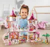 A young girl is smiling and playing with a large pink princess castle playset. Voir les images du produit