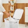 A person is putting a white towel into a white laundry basket in a bathroom. Produktbild-Vorschau