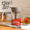 A funnel is being used to fill a jar with strawberry jam. There are also strawberries and a bowl in the background. Produktbild-Vorschau