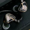 A close-up shot of two black in-ear monitor headphones with gold accents, resting on a textured black surface. Produktbild-Vorschau