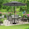 An outdoor patio set with a table, chairs, and an umbrella, surrounded by a garden with pink flowers. Produktbild-Vorschau