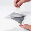 A person's hands are peeling a reflective film from a white surface. Produktbild-Vorschau