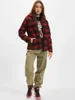 A woman stands in front of a white background wearing a red and black plaid jacket and green cargo pants. Produktbild-Vorschau