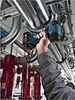 A person is using a Bosch cordless impact wrench to tighten a pipe fitting in an industrial or mechanical setting. Voir les images du produit
