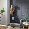 A white coat rack with a jacket and hat is shown in a room with a dresser, a couch, and a lamp. Produktbild-Vorschau