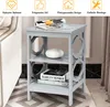 A gray three-tiered side table with decorative geometric cutouts on the sides, placed next to a sofa. Books and a vase are on the shelves. Podgląd zdjęcia produktu