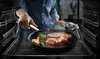 A person is cooking a steak in a pan inside an oven. Náhľad obrázku produktu