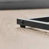 A close-up view of the black metal leg of a C-shaped side table resting on a light wood-grain surface. Produktbild-Vorschau
