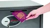 A hand is inserting a passport into a safe. Anteprima dell’immagine prodotto