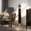 A tall, slender tower fan stands next to a chair in a softly lit room. Náhľad obrázku produktu