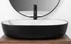 A close-up shot of a modern oval countertop sink with a black exterior and a marble-patterned interior, set against a plain white background with a reflection of a black faucet and a round mirror in the background. Náhľad obrázku produktu