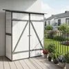 A white and gray wooden garden shed with double doors is shown on a wooden deck, with potted plants in front and houses in the background. Produktbild-Vorschau