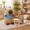 A young girl is playing with toys next to a large capybara plush toy in a room. Produktbild-Vorschau