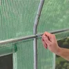 A close-up view of a person's hand adjusting a metal pole within a green, mesh-like greenhouse cover. Produktbild-Vorschau