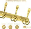 A golden coat rack with five hooks mounted on a gold plate. Text overlays highlight craftsmanship, finish, durability, strength, and heavy-duty load capacity. Produktbild-Vorschau