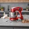 A red stand mixer is shown on a kitchen counter with baking ingredients and accessories. Produktbild-Vorschau