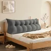 A bed with a large triangular pillow at the headboard, a blanket draped over the bed, and slippers on the floor.