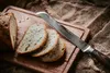 A loaf of bread is sliced on a wooden cutting board, with a serrated knife resting on top. Voir les images du produit