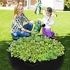 Schwarzes rundes Stoff-Hochbeet gefüllt mit grünem Salat, eine Frau und ein Mädchen gießen Pflanzen in einem Hinterhof Voir les images du produit