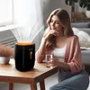 A woman sits at a wooden table next to a humidifier, holding a glass of water. Anteprima dell’immagine prodotto