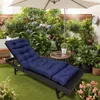 A navy blue chaise lounge cushion is placed on a black chaise lounge in a lush garden setting with many potted plants and an umbrella. Náhled obrázku produktu