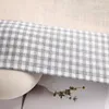 A close-up view of a checkered fabric with a white ribbed object and a sprig of dried flowers. Produktbild-Vorschau