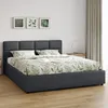 A dark gray upholstered bed with a botanical print duvet and pillows, set against a white wall with framed botanical prints and a light beige curtain. Produktbild-Vorschau