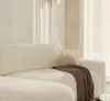 A close-up view of a cream-colored sectional sofa with a brown throw blanket and a small round cushion. Produktbild-Vorschau