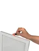 A hand is placing a heart-shaped decoration on the edge of a white picture frame. Produktbild-Vorschau