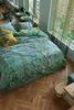 A bedroom scene with a bed dressed in a nature-themed duvet cover and pillows, near a window with curtains. Produktbild-Vorschau