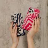 Two hands holding iPhone cases with a zebra-like pattern against a textured gray background. Náhled obrázku produktu