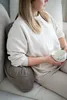 A person sitting on a couch with a backrest pillow and holding a bowl. Náhled obrázku produktu