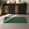 A dark wooden sideboard with decorative items on top, and a green rug on a gray floor, with sunlight streaming in. Produktbild-Vorschau