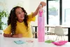 A young girl is holding a Barbie doll that is inside a tall, pink, glittery tube. Podgląd zdjęcia produktu