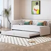 A beige daybed with an extended trundle bed, set up in a room with a potted plant and artwork on the wall. Produktbild-Vorschau