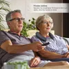 An older couple sitting on a couch watching TV, with the woman wearing a neck speaker. Produktbild-Vorschau