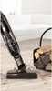 A cordless vacuum cleaner is shown on a wooden floor next to a basket of firewood. Voir les images du produit