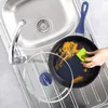 A hand is cleaning a frying pan with a sponge in a kitchen sink. Produktbild-Vorschau