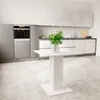 A modern kitchen with a white square table in the foreground and a plant in a vase on it. Produktbild-Vorschau