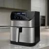 A silver and black air fryer is shown on a kitchen counter with dimensions indicated. Produktbild-Vorschau